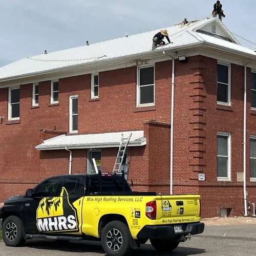 Roofing crew on metal roof with safety lines and branded truck — commercial roof replacement guide by Mile High Roofing Services in Westminster, CO